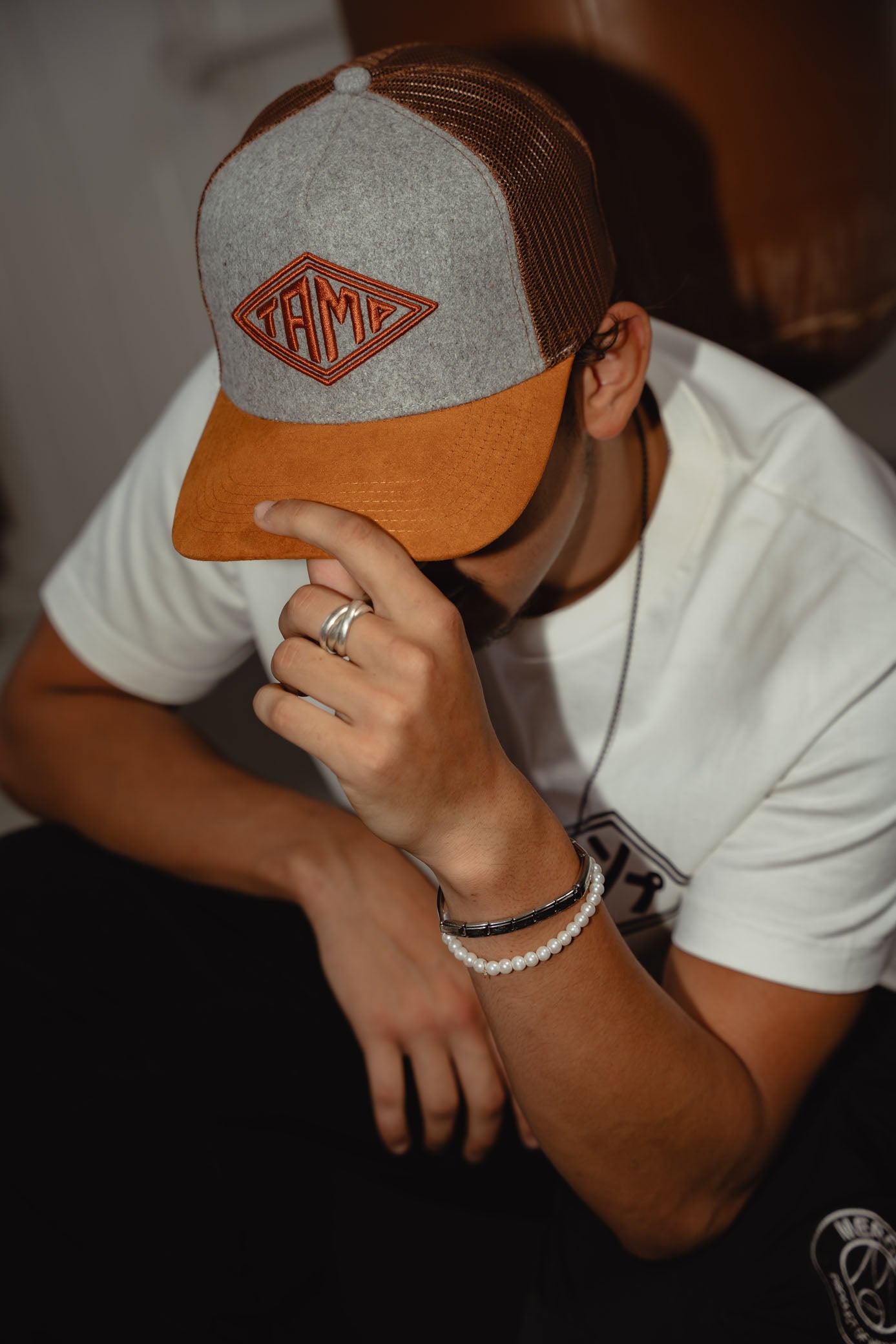 Model wearing grey trucker cap with brown mesh and brown Tamp Coffee logo