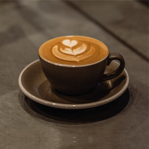 A visually captivating Cup of Specialty Coffee showcasing a stunning rosetta design gracefully etched into the frothy milk, elegantly presented on a modern grey plate atop a sleek surface
