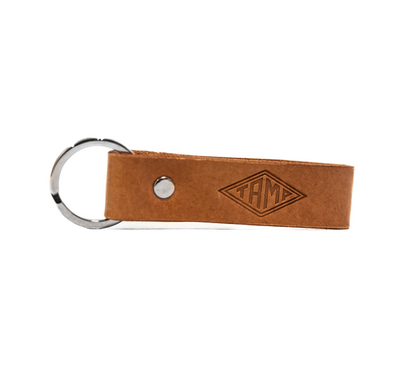 front view of a handcrafted natural brown leather keyring from Tamp Coffee, featuring intricate stitching and embossed logo detail