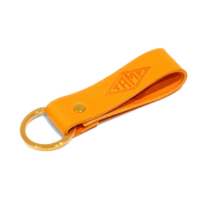 close-up view of a handcrafted orange leather keyring from Tamp Coffee, featuring intricate stitching and embossed logo detail